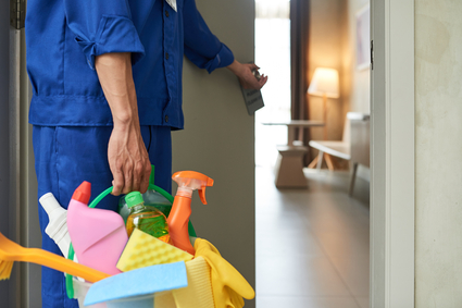 unrecognizable cleaner walking into hotel room with tools detergents